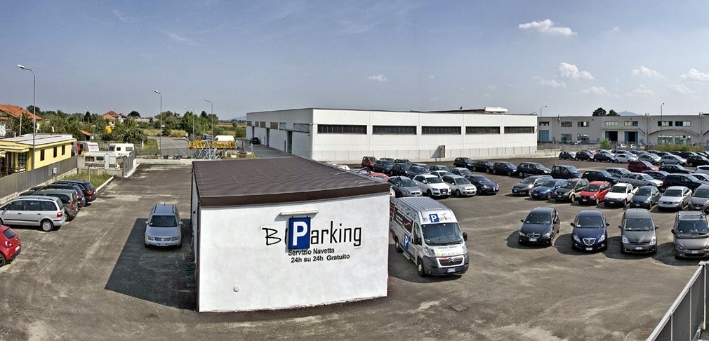 Il piazzale pieno di auto e l'ufficio con la scritta Servizio navetta 24h su 24h gratuito